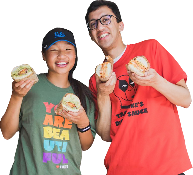 Two smiling people holding sandwich halves.